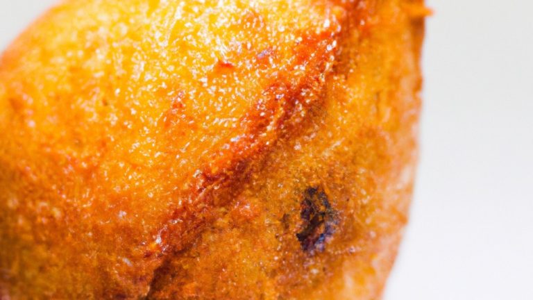 Fotografia de uma coxinha da asa assada em uma fritadeira elétrica. A coxinha é dourada e crocante, com a pele torrada e suculenta. O fundo é branco, com a fritadeira elétrica visível no canto inferior direito.