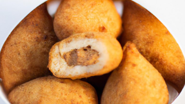 Imagem de uma coxinha de frango com batata frita em uma fritadeira AirFryer. A coxinha é marrom dourada e crocante, com uma batata frita crocante do lado. O fundo da imagem é uma mesa de madeira com um pano de prato xadrez vermelho e branco.