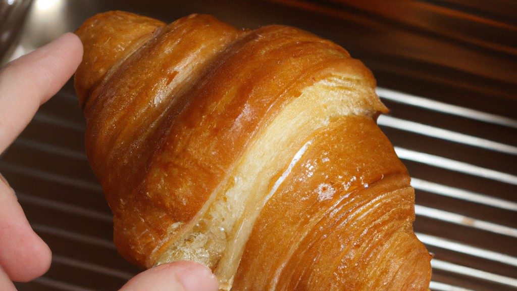 Imagem de croissants congelados dourados e crocantes cozidos em uma Airfryer, colocados em um prato com manteiga derretida ao lado.