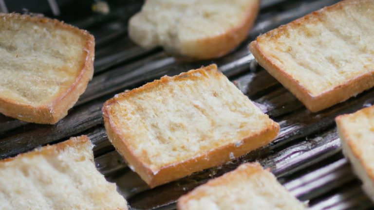 Imagem de crostinis de tapioca feitos na airfryer. Os crostinis são crocantes e dourados, cobertos com uma mistura de atum, tomate, cebola roxa e azeitonas pretas.