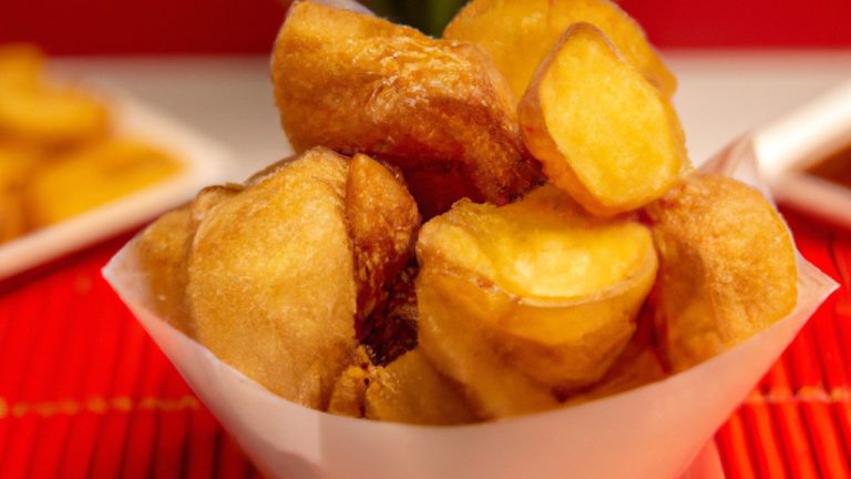 Imagem de dadinhos de mandioca dourados e crocantes cozidos em uma airfryer, com um molho de pimenta à parte.