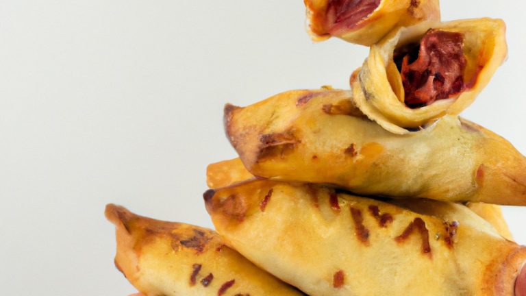 Fotografia de um enroladinho dourado crocante feito com massa de pastel cozida na airfryer. O enroladinho está cortado ao meio, revelando um recheio farto e fumegante.