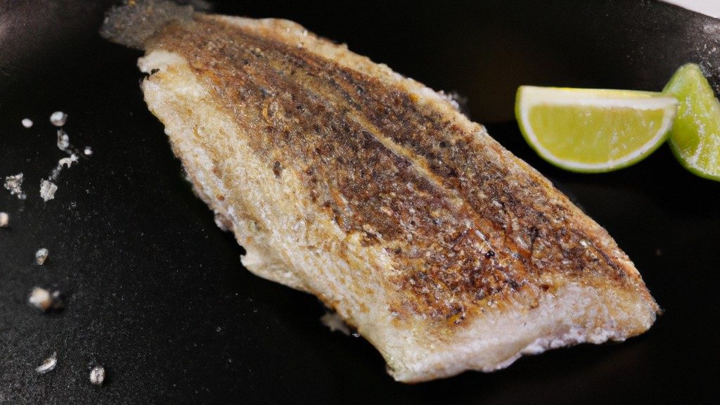 Foto de um prato com filé de merluza crocante e dourado, preparado na airfryer. A merluza é servida com fatias de limão e ervas frescas, como salsa e cebolinha. O fundo da imagem mostra uma airfryer aberta, indicando que o peixe foi cozido neste aparelho.