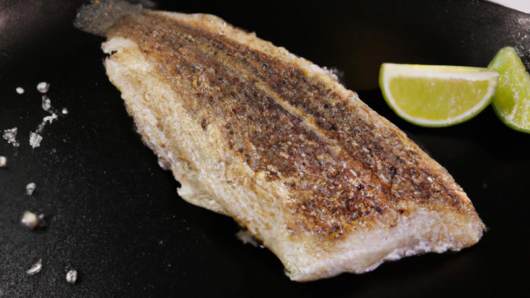 Foto de um prato com filé de merluza crocante e dourado, preparado na airfryer. A merluza é servida com fatias de limão e ervas frescas, como salsa e cebolinha. O fundo da imagem mostra uma airfryer aberta, indicando que o peixe foi cozido neste aparelho.