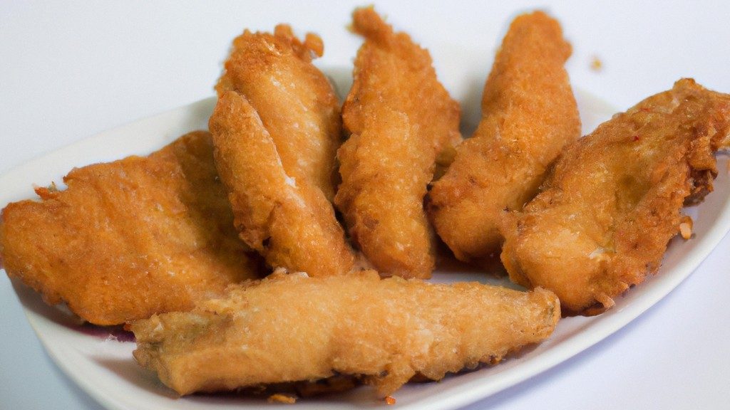 Imagem de filés de peixe empanados crocantes e dourados em um prato branco, servidos com rodelas de limão e molho tártaro.