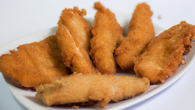 Imagem de filés de peixe empanados crocantes e dourados em um prato branco, servidos com rodelas de limão e molho tártaro.
