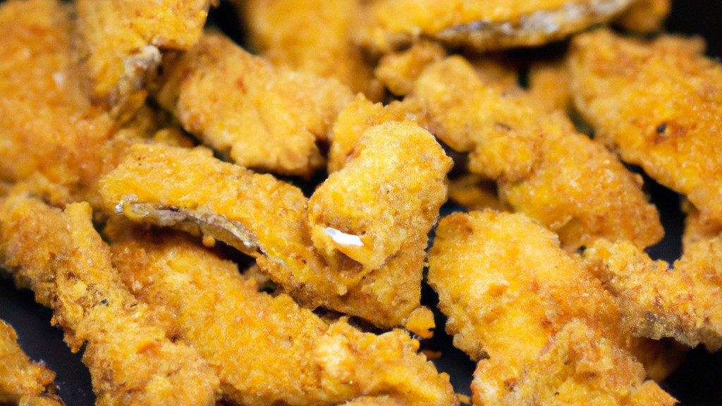 Imagem de filés de pescada empanados dourados e crocantes dispostos em uma cesta de airfryer. Os filés são servidos com fatias de limão e um ramekin de molho tártaro.