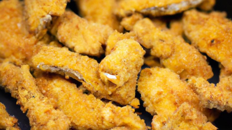 Imagem de filés de pescada empanados dourados e crocantes dispostos em uma cesta de airfryer. Os filés são servidos com fatias de limão e um ramekin de molho tártaro.