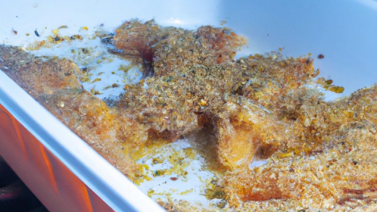 Imagem de uma fritadeira elétrica contendo frango empanado com ervas. O frango está dourado e crocante, com ervas visíveis na superfície. A fritadeira está sobre uma superfície preta, com um fundo desfocado.