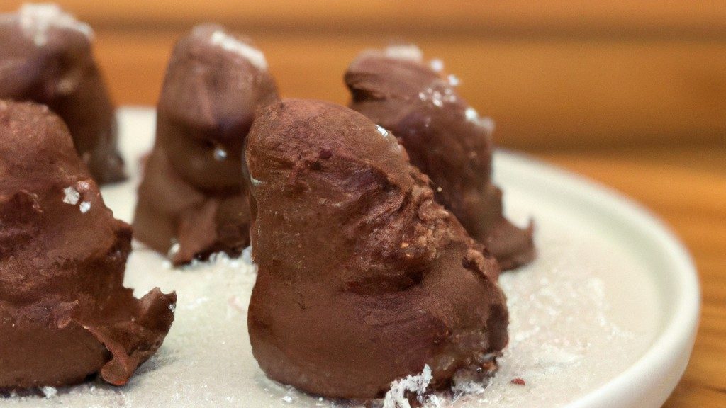 Imagem de uma cesta de fritadeira cheia de fudge de varinha de chocolate, com os topos salpicados de granulado de arco-íris. O fudge é marrom escuro e brilhante, com uma textura lisa e cremosa. É cortado em quadrados e disposto em linhas ordenadas na cesta. O fundo é branco, com o texto "Fudge da Varinha Na Airfryer: Receita Fácil E Deliciosa" escrito em preto na parte superior.