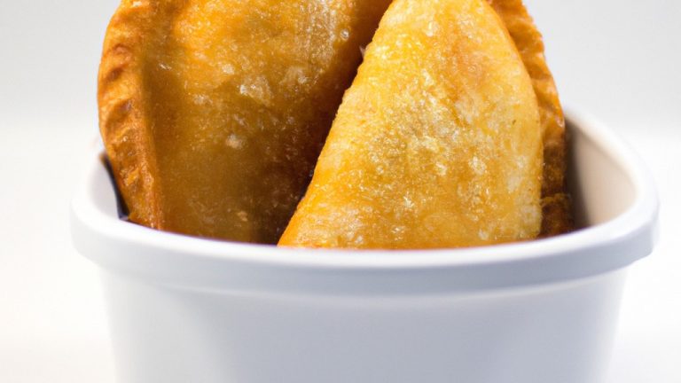 Imagem de empanadas douradas e crocantes, preparadas na Airfryer. As empanadas têm um recheio saboroso, visível através das bordas abertas. Elas são servidas em um prato com um molho de acompanhamento.