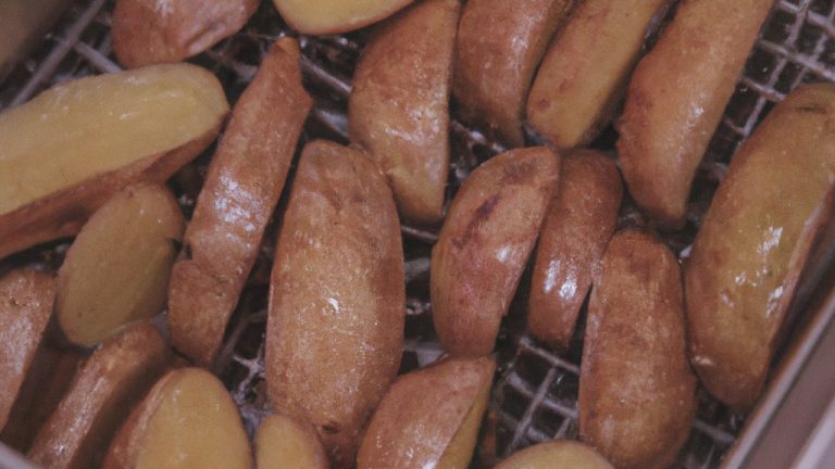 Imagem de lascas de batata-doce douradas e crocantes organizadas em uma cesta de fritadeira. Elas estão decoradas com sal marinho e ervas frescas.