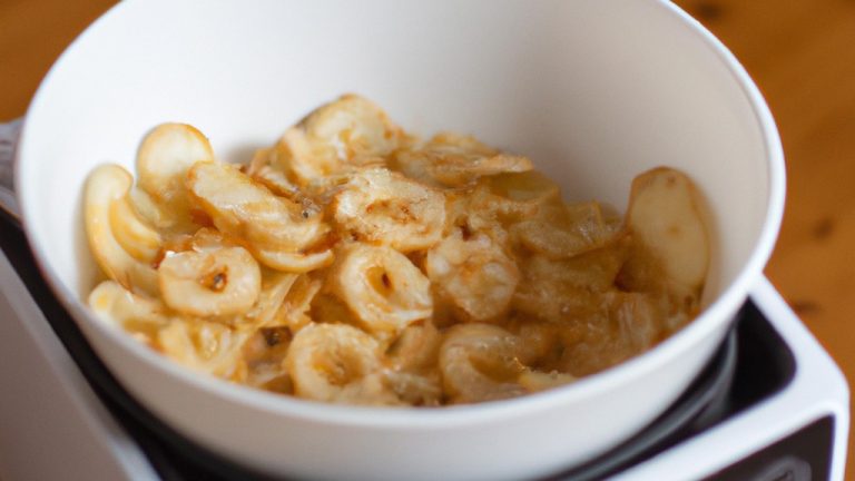 Imagem mostra um prato de macarrão cremoso cozido em uma Airfryer, ao lado de ingredientes como leite, creme de leite, queijo parmesão e macarrão.