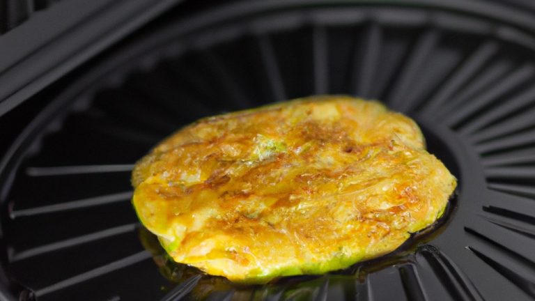 Imagem de uma omelete de abobrinha frita ao ar, cortada em fatias e servida em um prato. A omelete é dourada e crocante por fora e macia e suculenta por dentro.