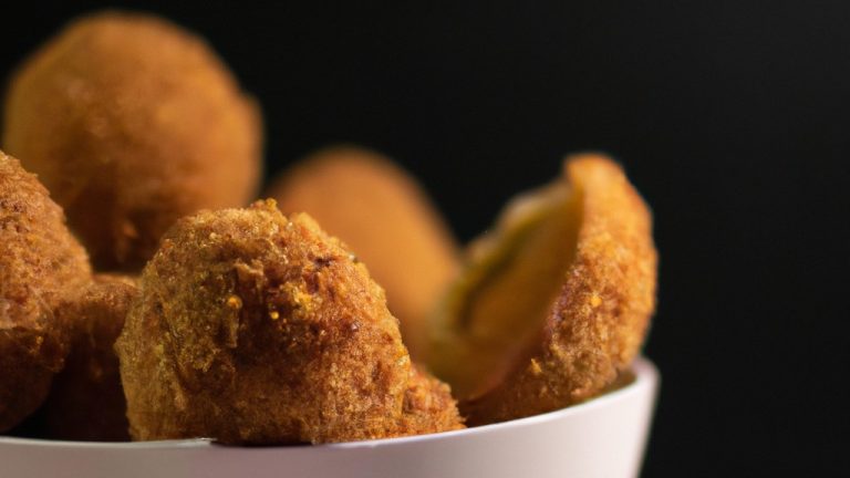 Uma fotografia de cima de um prato cheio de ovos empanados, dourados e crocantes, feitos na Airfryer. Os ovos estão cortados ao meio, revelando uma gema cozida perfeitamente. O prato é guarnecido com fatias de limão e ervas frescas.