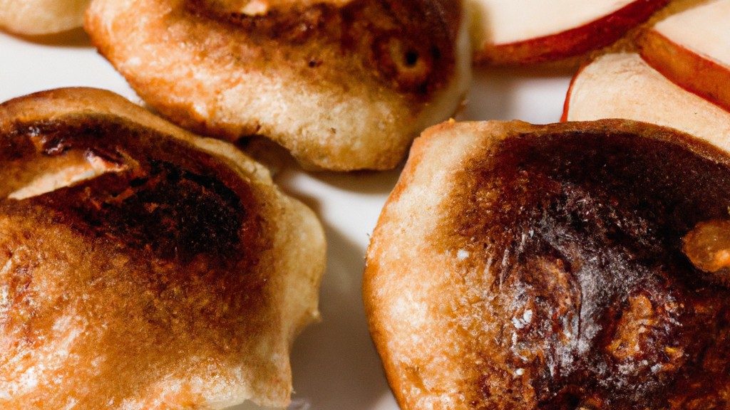 Imagem de panquecas de maçã douradas e fofas preparadas na Airfryer. A pilha de panquecas é decorada com pedaços de maçã caramelizados e servida com calda de bordo ao lado.