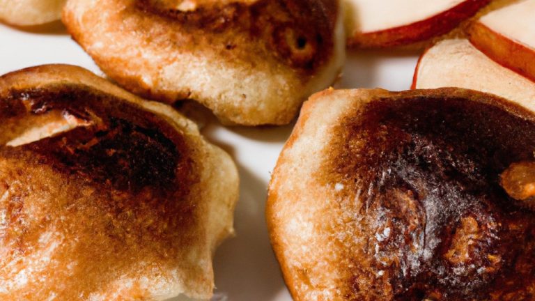 Imagem de panquecas de maçã douradas e fofas preparadas na Airfryer. A pilha de panquecas é decorada com pedaços de maçã caramelizados e servida com calda de bordo ao lado.