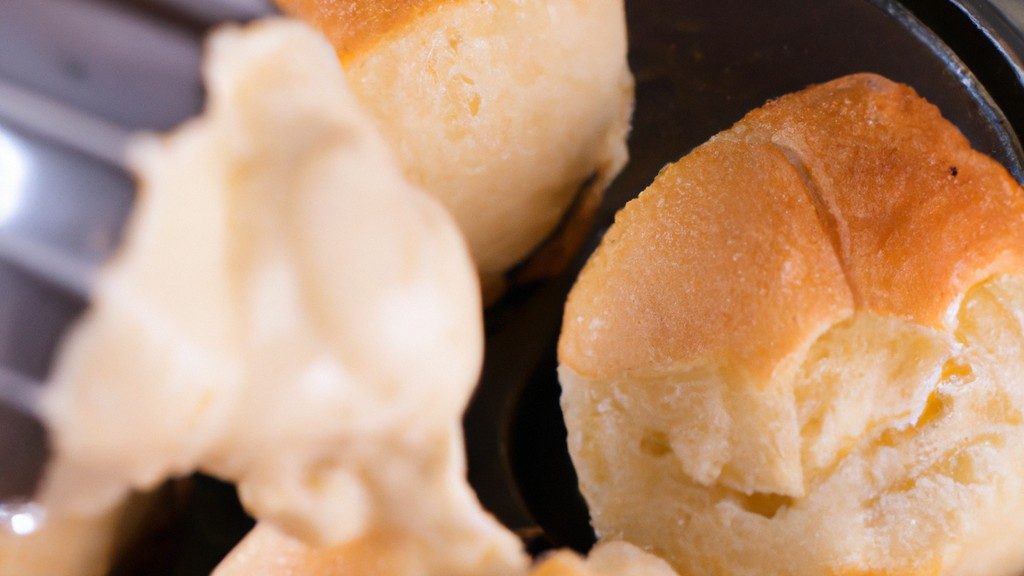 Imagem de uma cesta de Airfryer cheia de pão de queijo assados e dourados. Eles têm uma crosta crocante e um interior macio e esponjoso. Os pães de queijo são servidos em um prato com um lado de molho de tomate.