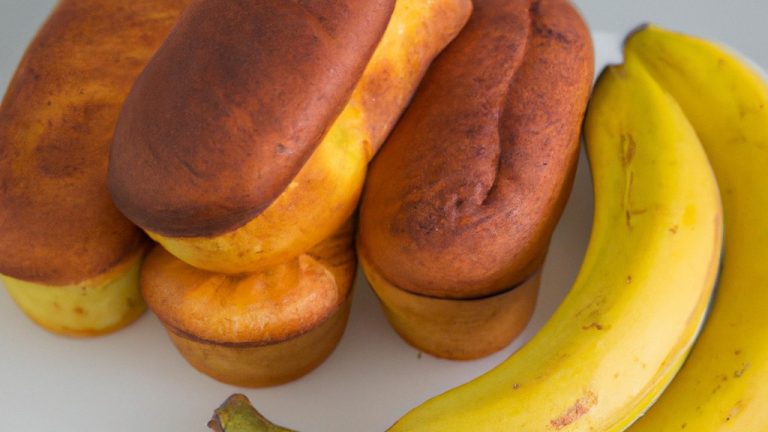 Imagem de pão de forma com banana preparado na airfryer. O pão está cortado em quadrados e tem uma cor dourada. Ele é servido em um prato branco com uma fatia de banana ao lado.