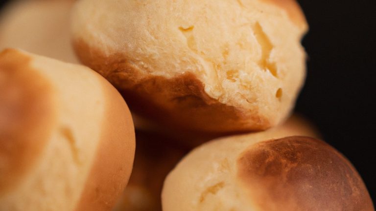 Imagem de um pão de leite dourado e crocante cozido em uma airfryer. A casca é ligeiramente crocante e o miolo é macio e fofo. O pão é colocado em uma tábua de madeira com uma faca ao lado.