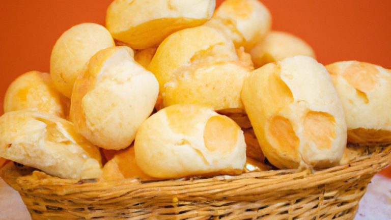 Imagem mostra uma cesta de pãozinho de batata sem glúten quentinhos e dourados. Os pães têm uma crosta crocante e um miolo macio e fofo. A cesta está sobre uma toalha de mesa branca e o fundo é desfocado.