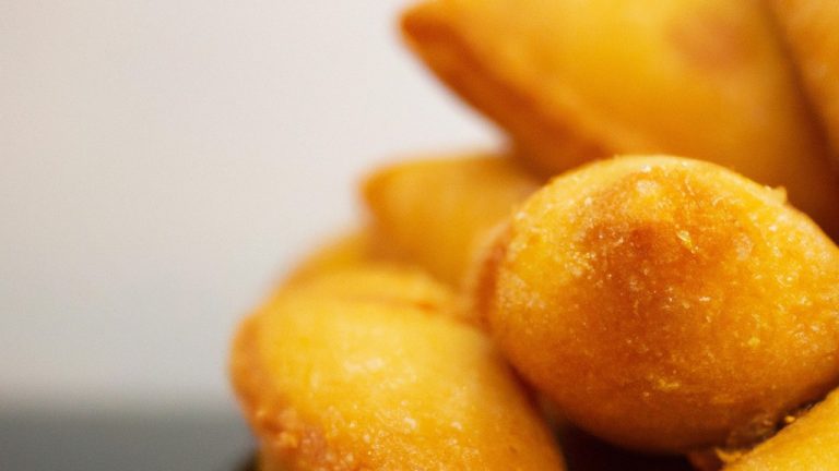 Imagem de pastéis de queijo assados na Airfryer, com uma crosta dourada e crocante. Eles estão dispostos em um prato branco, com uma tigela de molho ao lado.