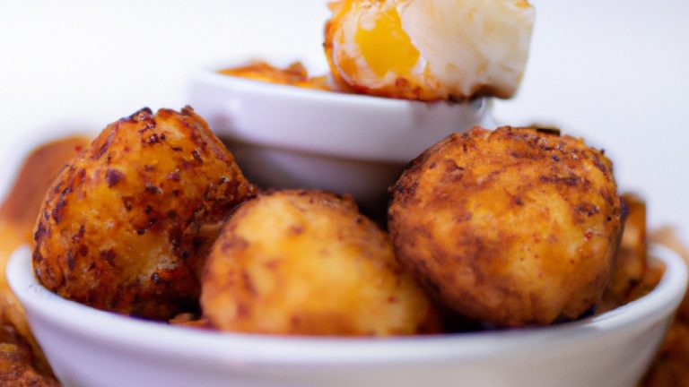 Uma foto de cima para baixo de bolinhos de batata doce e frango fritos em uma airfryer. Os bolinhos são dourados e crocantes, com um interior macio e fofo. Eles são servidos em um prato com um molho de iogurte ao lado.