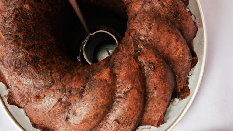 Imagem de um bolo de chocolate assado em uma airfryer. O bolo é coberto com cobertura de chocolate e tem uma colher ao lado.