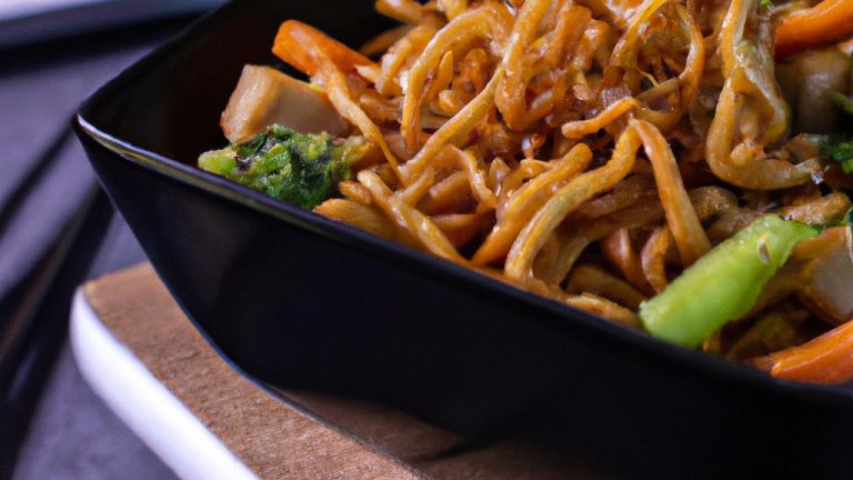 Imagem de yakisoba crocante preparado em uma airfryer. O macarrão é coberto com vegetais, carne e um molho escuro. O yakisoba está em um prato branco e é guarnecido com cebolinha e gergelim.