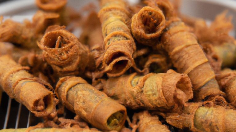 Imagem mostra um rolinho de abobrinha crocante cozido na airfryer. O rolinho é dourado e crocante, recheado com uma mistura de queijo, vegetais e especiarias. O rolinho é apresentado num prato com uma fatia de limão ao lado.