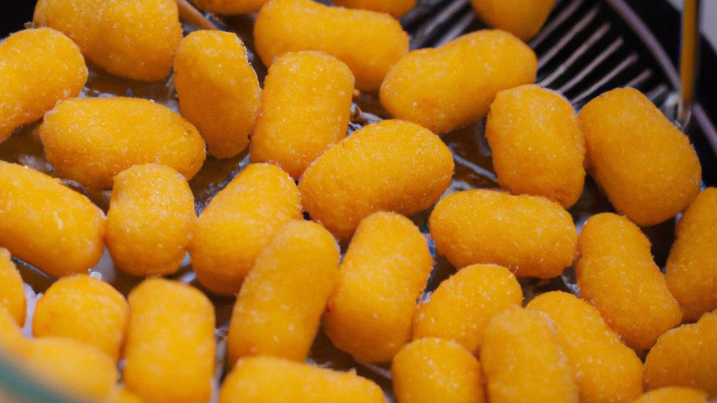 Imagem de salgadinhos de queijo crocantes e dourados preparados na airfryer. Os salgadinhos têm uma forma triangular e são cobertos com queijo derretido e borbulhante. Eles estão dispostos em um prato forrado com papel manteiga.