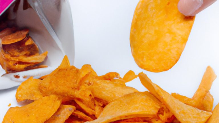 Imagem de chips de batata doce crocantes e dourados preparados em uma Airfryer. As batatas doces são cortadas em fatias finas e empilhadas em uma cesta de Airfryer. O fundo da imagem mostra uma tábua de cortar com uma faca e uma tigela de batatas doces fatiadas.