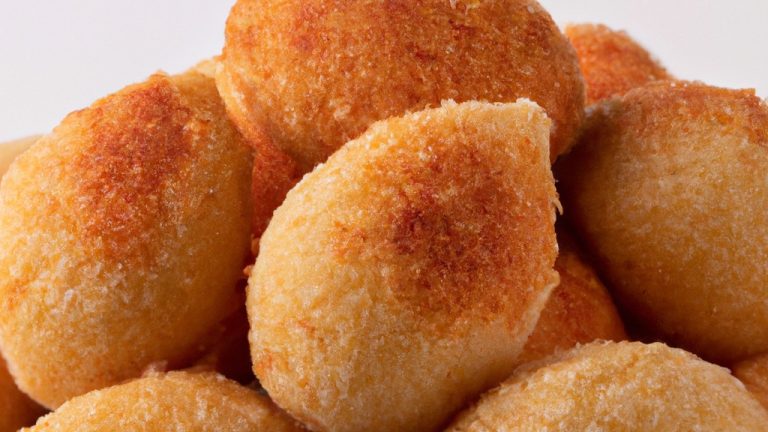 Uma imagem de bolinhos de arroz crocantes e dourados feitos na Airfryer. Os bolinhos são servidos em um prato com um molho de imersão à parte. O fundo é desfocado, destacando os bolinhos na frente.