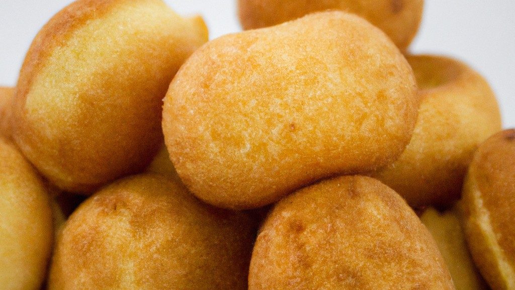 Imagem de um bolinho de estudante recém-feito em uma airfryer. O bolinho é dourado e tem uma cobertura de chocolate derretido. Está em uma cesta de airfryer com papel manteiga.
