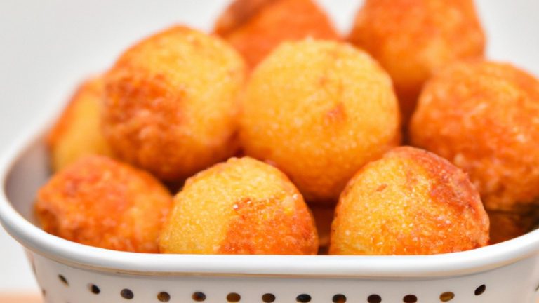 Imagem de bolinhos dourados e crocantes em forma de bola, feitos com risoto restante e revestidos com farinha de rosca. Os bolinhos são servidos em um prato branco com um molho de tomate ao lado.