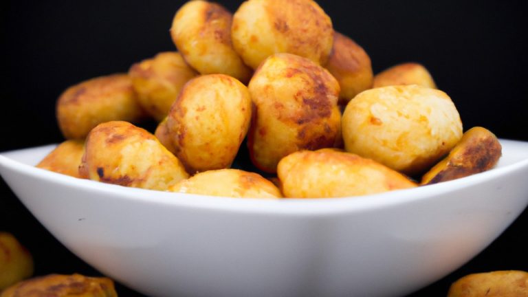 Foto de bolinhos de batata com calabresa cozidos na Airfryer. Os bolinhos têm formato redondo e estão dourados. São servidos em um prato com uma tigela de molho de tomate ao lado.