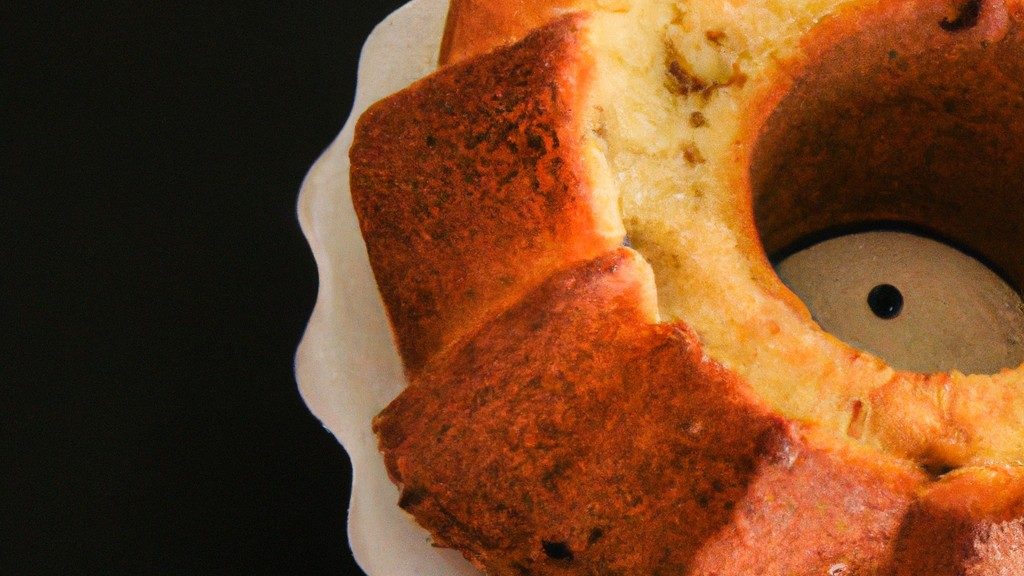 Imagem de um bolo redondo e dourado cozido em uma airfryer. O bolo é coberto com uma cobertura de chocolate e granulado colorido.