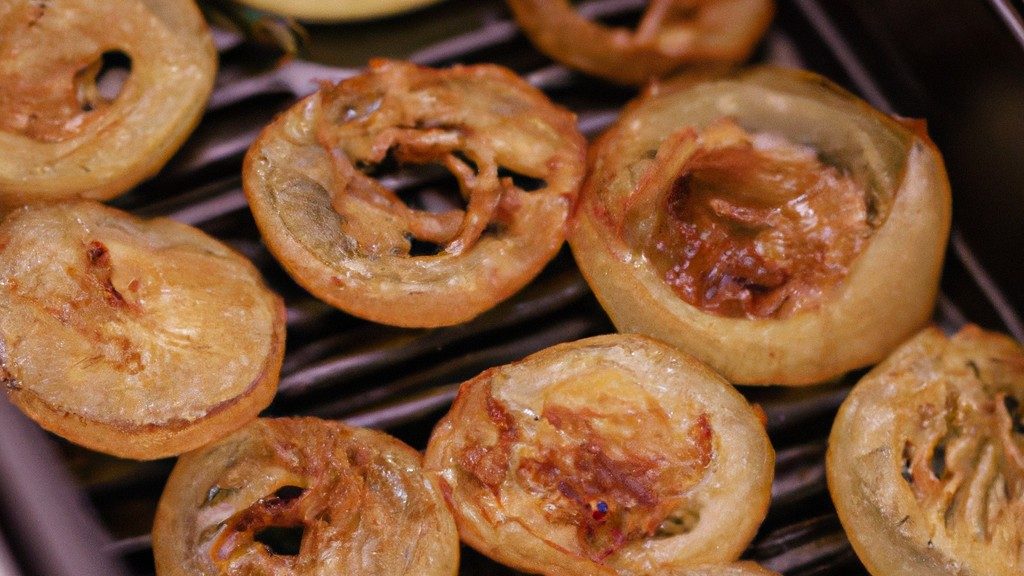 Imagem de uma cebola assada na Airfryer. A cebola é marrom-dourada e tem uma textura crocante. É cortada em rodelas e colocada numa travessa.