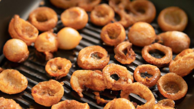 Imagem de cebolas caramelizadas crocantes e douradas preparadas na Airfryer. As cebolas são cortadas em fatias finas e caramelizadas até ficarem macias e ligeiramente crocantes. Elas têm uma cor marrom-dourada escura e são polvilhadas com ervas frescas para adicionar sabor. A imagem mostra o processo de cozimento das cebolas na Airfryer, com as fatias de cebola espalhadas na cesta da fritadeira.