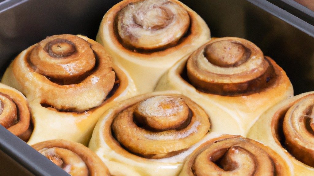 Imagem mostra uma cesta de fritadeira cheia de rolinhos de canela dourados e crocantes, polvilhados com uma generosa camada de cobertura de cream cheese. Os rolinhos são macios e fofos por dentro, com um aroma doce e irresistível.