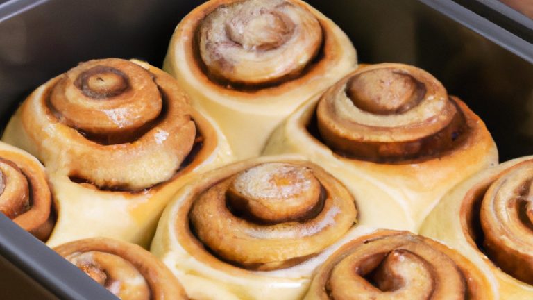 Imagem mostra uma cesta de fritadeira cheia de rolinhos de canela dourados e crocantes, polvilhados com uma generosa camada de cobertura de cream cheese. Os rolinhos são macios e fofos por dentro, com um aroma doce e irresistível.