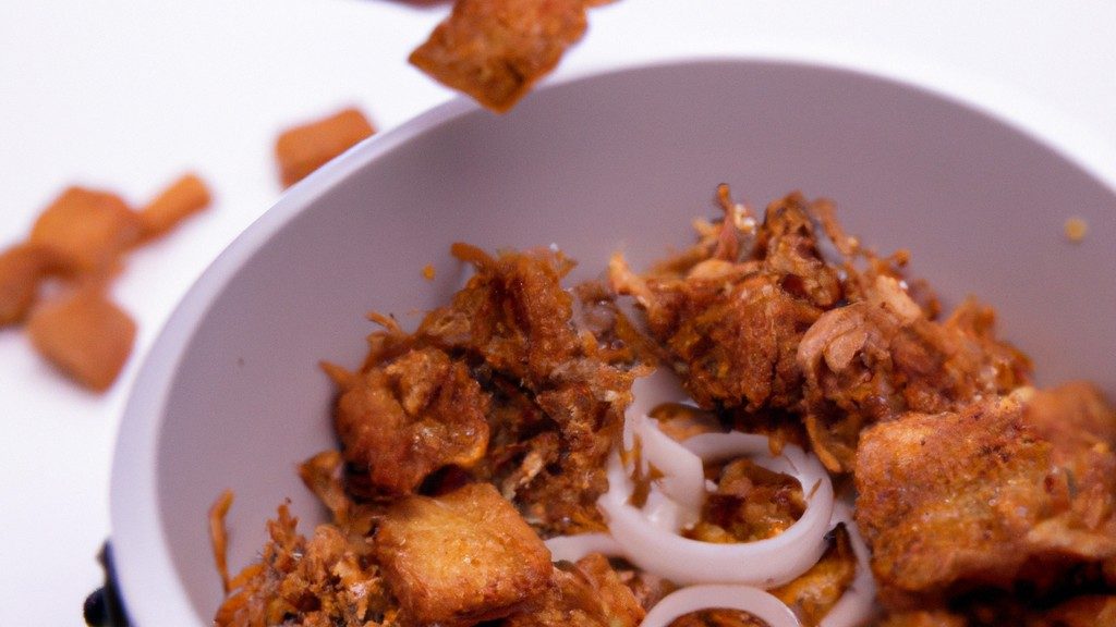 Imagem de cebolas crocantes fritas na Airfryer em um prato branco. As cebolas são cortadas em rodelas e cobertas com uma camada crocante dourada. A Airfryer é mostrada ao fundo, com a cesta aberta mostrando as cebolas cozidas.