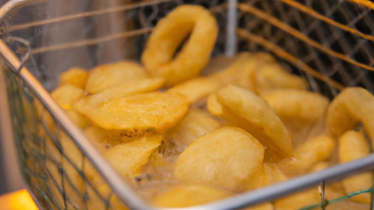 Imagem de uma porção de macaxeira frita crocante em uma airfryer. As macaxeiras estão cortadas em palitos e douradas, com sal e temperos polvilhados por cima.