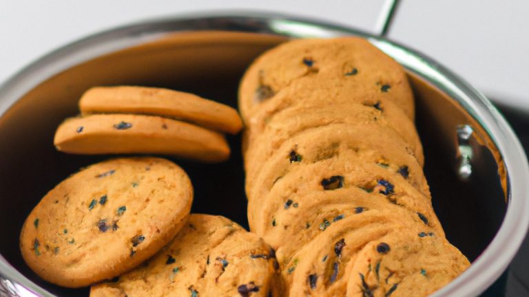 Imagem de uma cesta de fritadeira cheia de cookies recém-assados. Os cookies são dourados e crocantes, com gotas de chocolate derretidas na superfície. A fritadeira está colocada sobre uma bancada de cozinha com uma tábua de corte e uma faca ao lado.