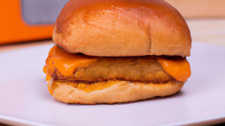 Imagem de um delicioso hambúrguer de frango recém-preparado em uma Airfryer. O hambúrguer é empanado com farinha de rosca crocante e dourada, e coberto com queijo derretido, alface fresca, tomate e cebola roxa. O fundo da imagem mostra a cesta da Airfryer, com o hambúrguer perfeitamente cozido e suculento.