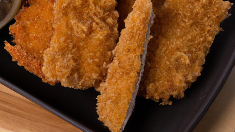 Imagem mostra lombinho empanado frito na airfryer, cortado em tiras finas e douradas, com uma crosta crocante e uma carne macia e suculenta no interior. O prato é servido com um molho cremoso ao lado, acompanhado de salada verde fresca.