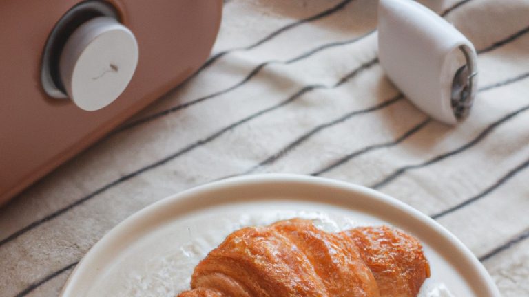 Imagem de mini croissants dourados e crocantes recém-saídos da airfryer, servidos em um prato branco com uma tigela de geléia de framboesa ao lado.