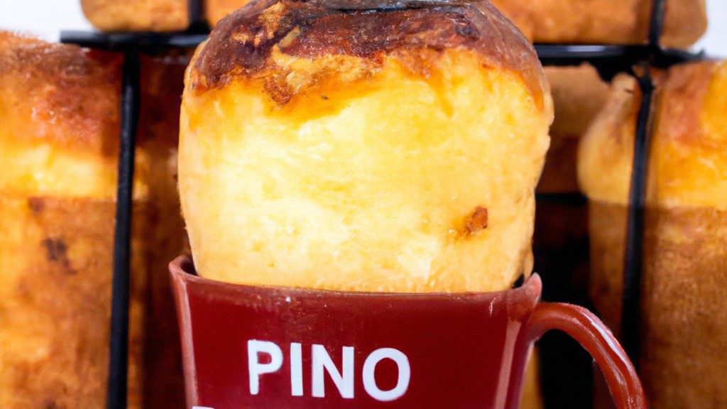 Imagem de um panetone de caneca na Airfryer. O panetone é marrom dourado e tem uma textura fofa, com uma cobertura de açúcar de confeiteiro polvilhada por cima. A caneca é branca e tem uma alça vermelha. Ao fundo, há uma Airfryer preta.