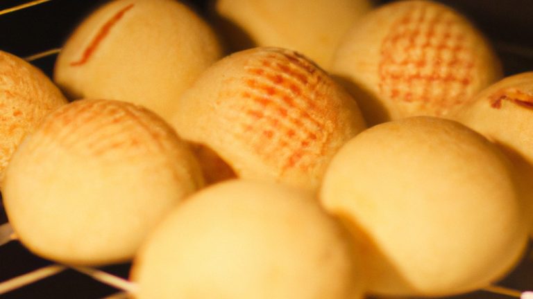 Pão de queijo crocante e dourado feito em uma Airfryer. Os pães de queijo são redondos e apresentam uma crosta exterior marrom-dourada, enquanto o interior é macio e arejado. Eles são servidos em um prato branco com uma tigela de molho de tomate ao lado.