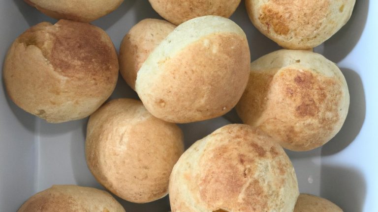Imagem aérea de um prato redondo cheio de pães de queijo dourados e crocantes, recém-saídos da airfryer. Os pães de queijo têm uma crosta crocante e um interior macio e amanteigado, e são polvilhados com parmesão ralado.